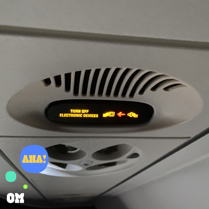 Momentos of magic in the mundane. A picture of the interior of a commercial airplane with the notification sign to turn off electronic devices and buckle your seatbelt.